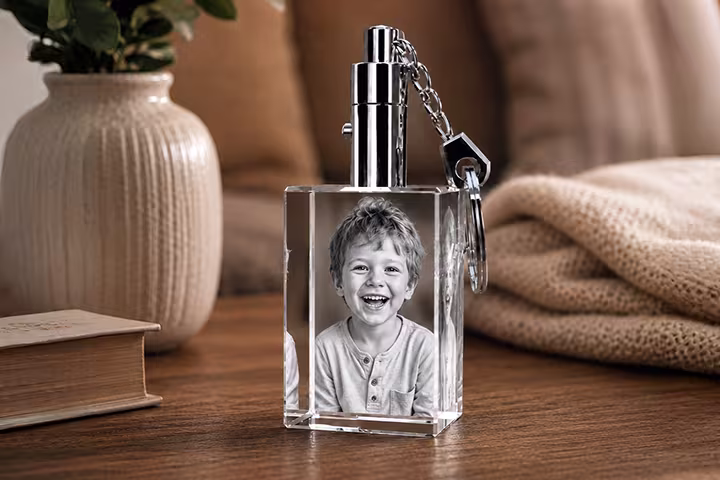 2D Crystal Rectangle Keychain engraved with a smiling young boy portrait, featuring a polished metal key ring on a cozy wooden tabletop.