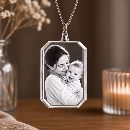 2D Crystal Rectangle Necklace engraved with a mother and baby portrait, suspended from a silver chain beside a glowing candle.