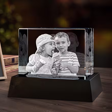 Wide Rectangle 3D Photo Crystal engraved with two children sharing ice cream, displayed on a black LED light base beside the original photo.