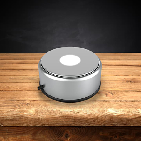Round silver rotating LED light base on a wooden table